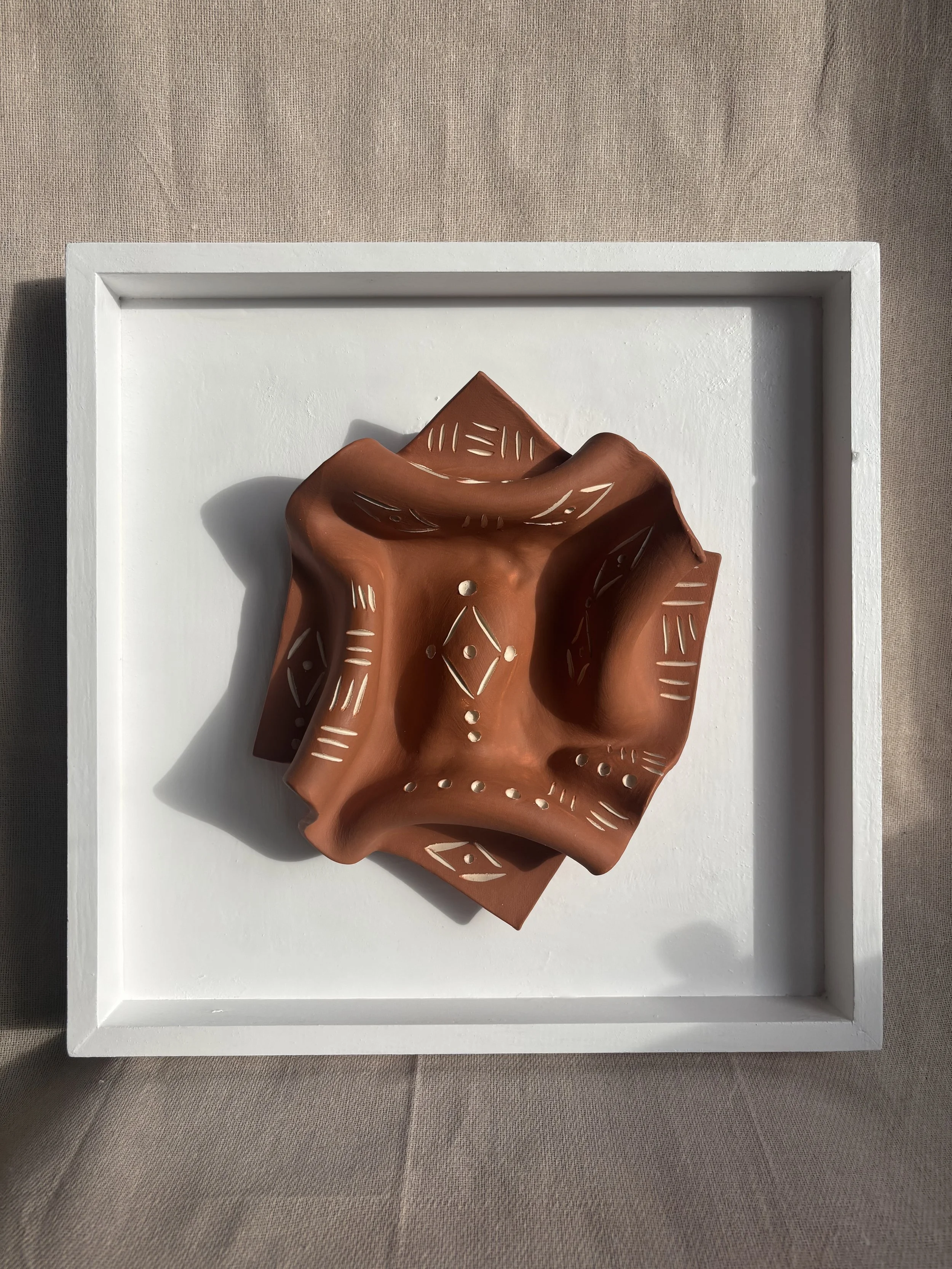 A wired clay sculpture with cut-out patterns placed on a white platform against a beige textured background.
