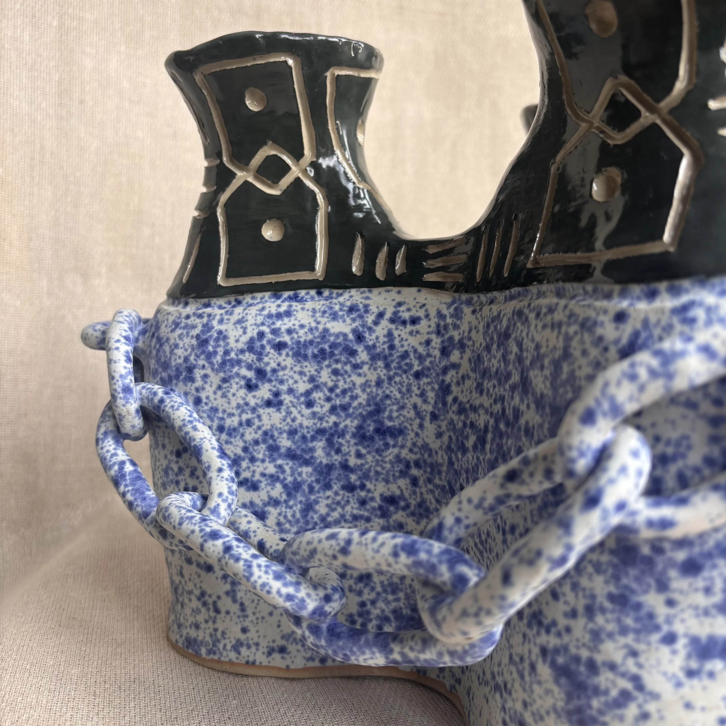 A ceramic table lamp with a blue speckled glaze and beige trim, placed on a textured cloth surface.