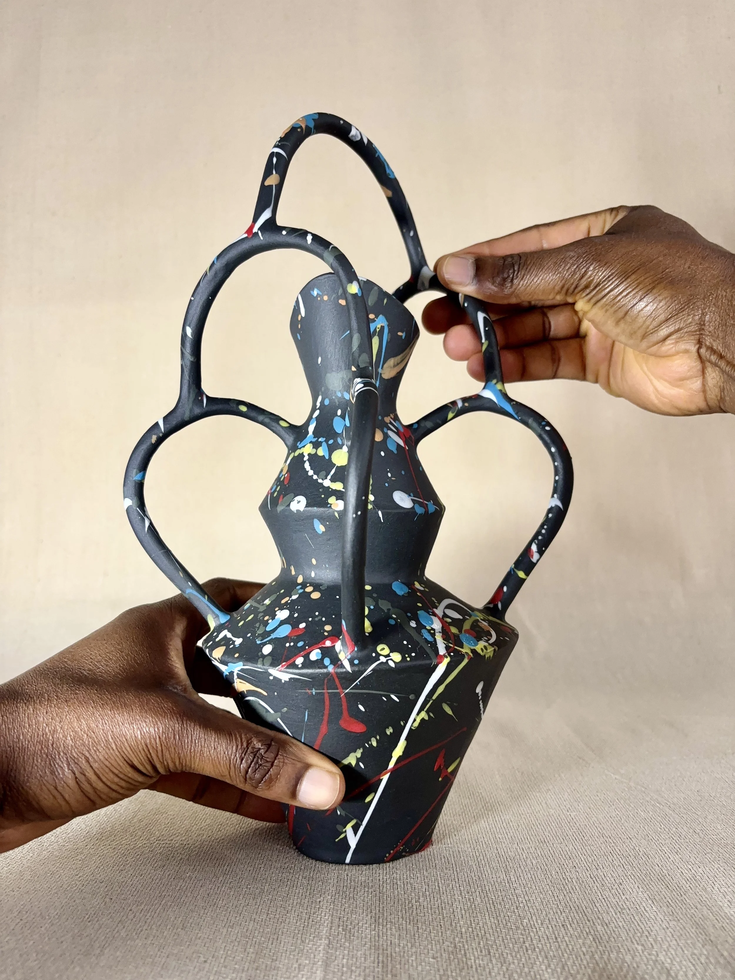 A person holding a black decorative sculpture with colorful paint splatters, featuring a lattice design with rounded and pointed elements.
