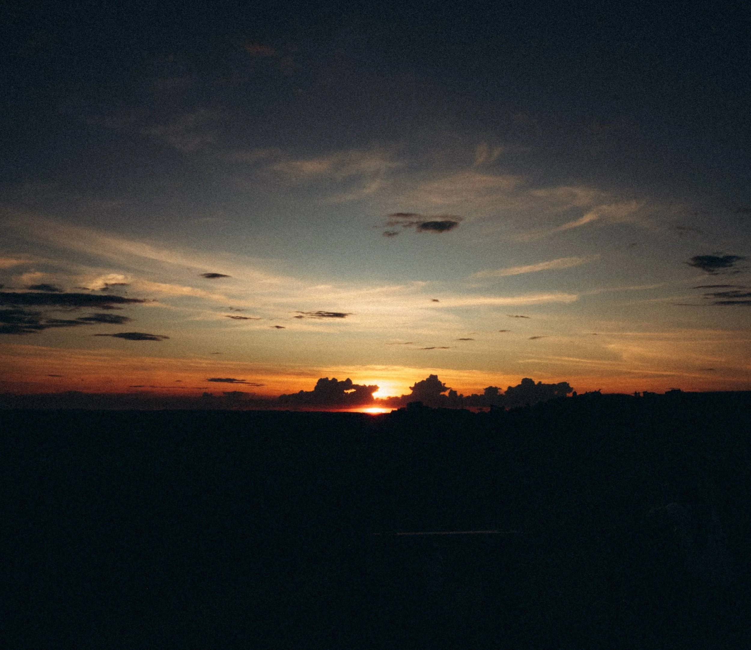 A sunset or sunrise over a horizon with scattered clouds in the sky.