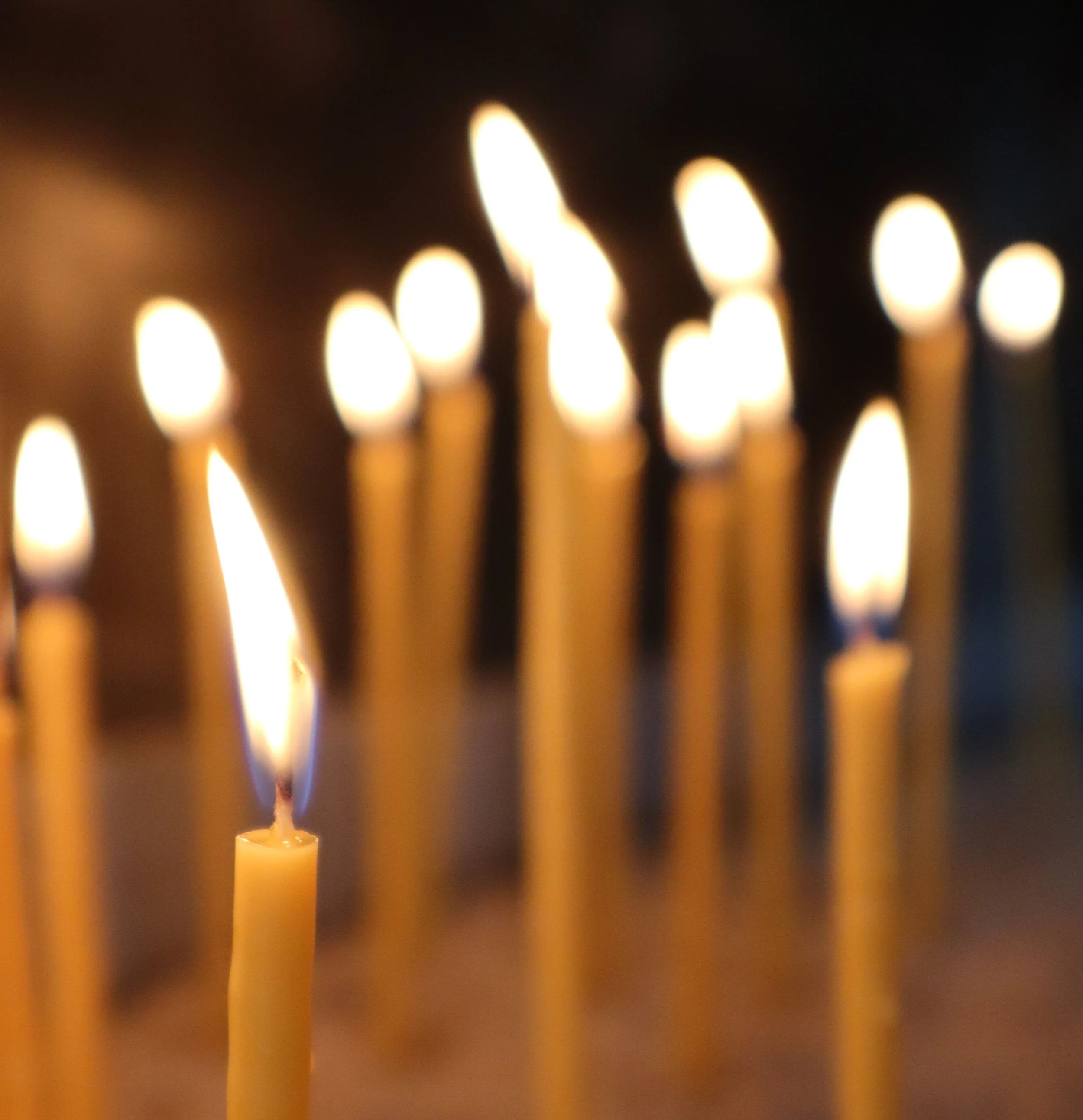 Close-up of several lit candles with warm orange and yellow flames against a dark background.