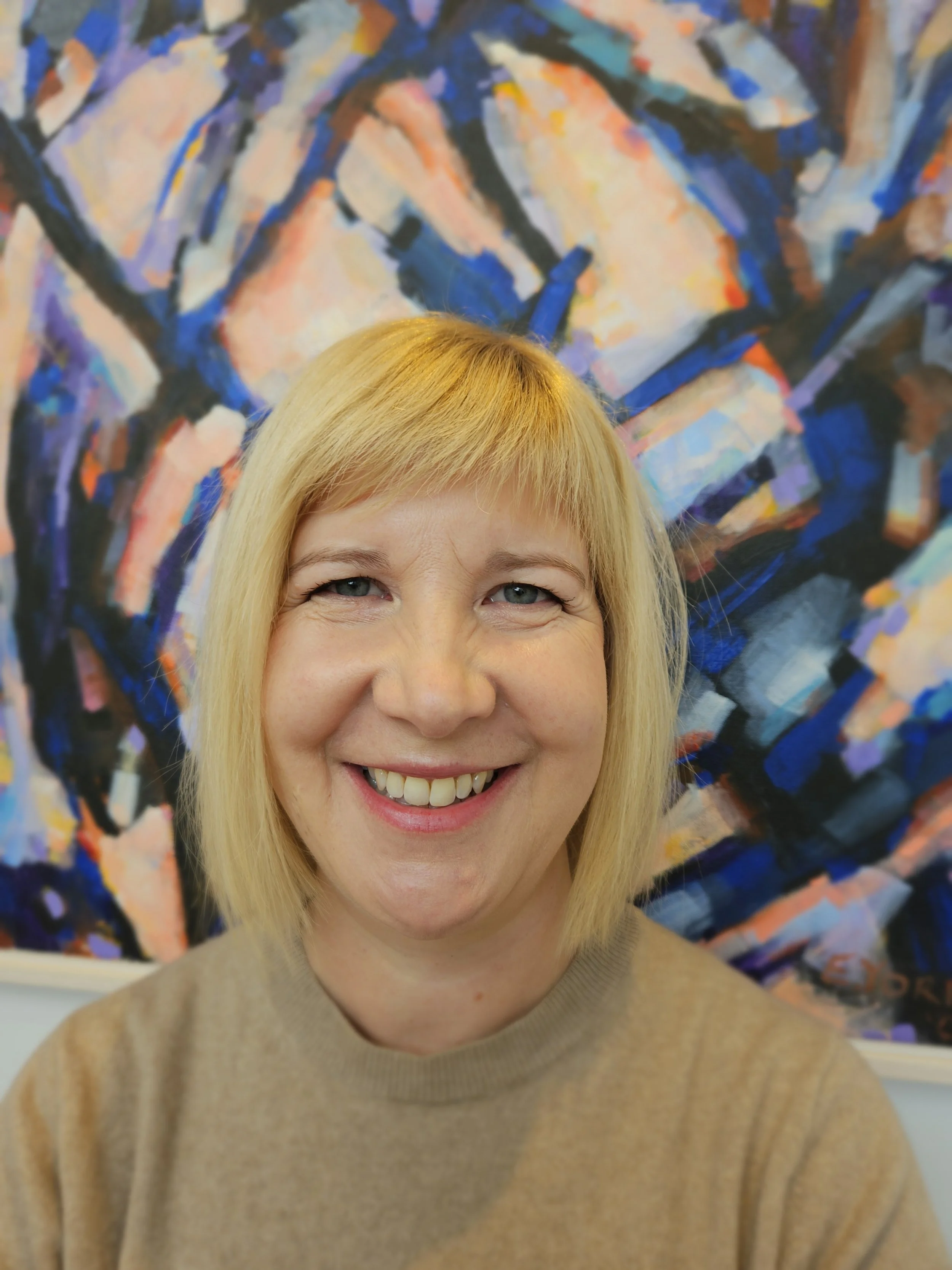 Close-up of Sarah Black in front of an abstract colourful painting.