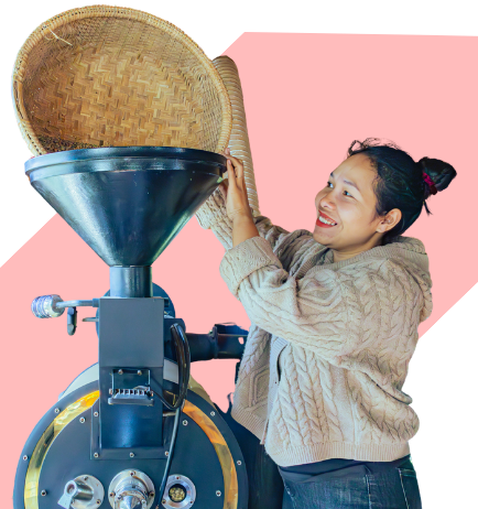 A woman operating a rice milling machine, pouring rice from a woven basket into the machine's hopper.