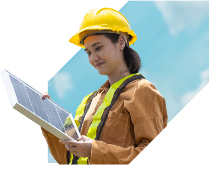 A woman in a yellow hard hat and safety vest holding a solar panel outdoors with a blue sky background.