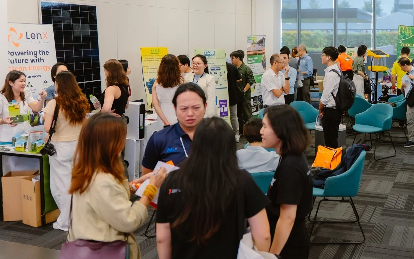 Attendees at an indoor tech or energy conference, talking and exploring booths with informational posters and displays.