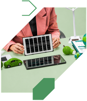Person in a pink blazer holding a tablet with solar panel images, surrounded by green toy cars, a green microphone, and documents on a desk, with a green wall in the background.