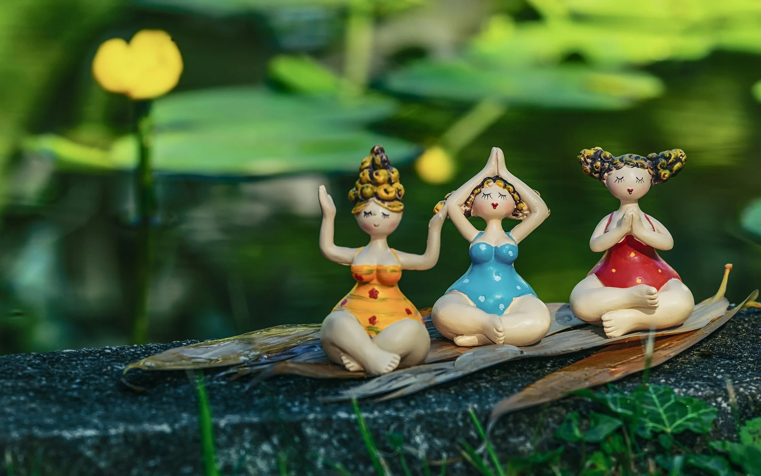 Tre keramikkfigurer av kvinner som meditasjon, plassert på en bladformet plattform ute i naturen.