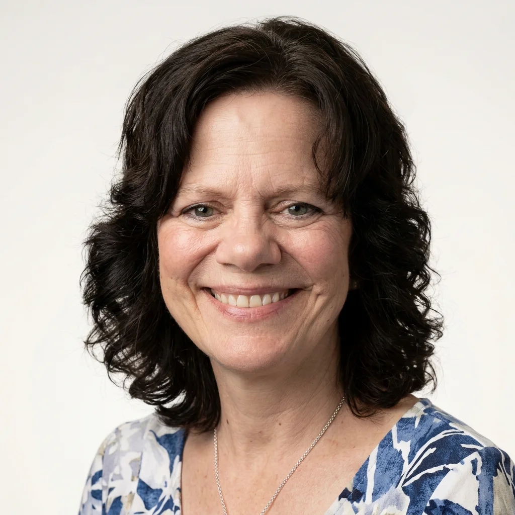 Portrett av en smilende kvinne med mørkt, krøllete hår, iført blå og hvit mønstret topp, mot en lys bakgrunn.