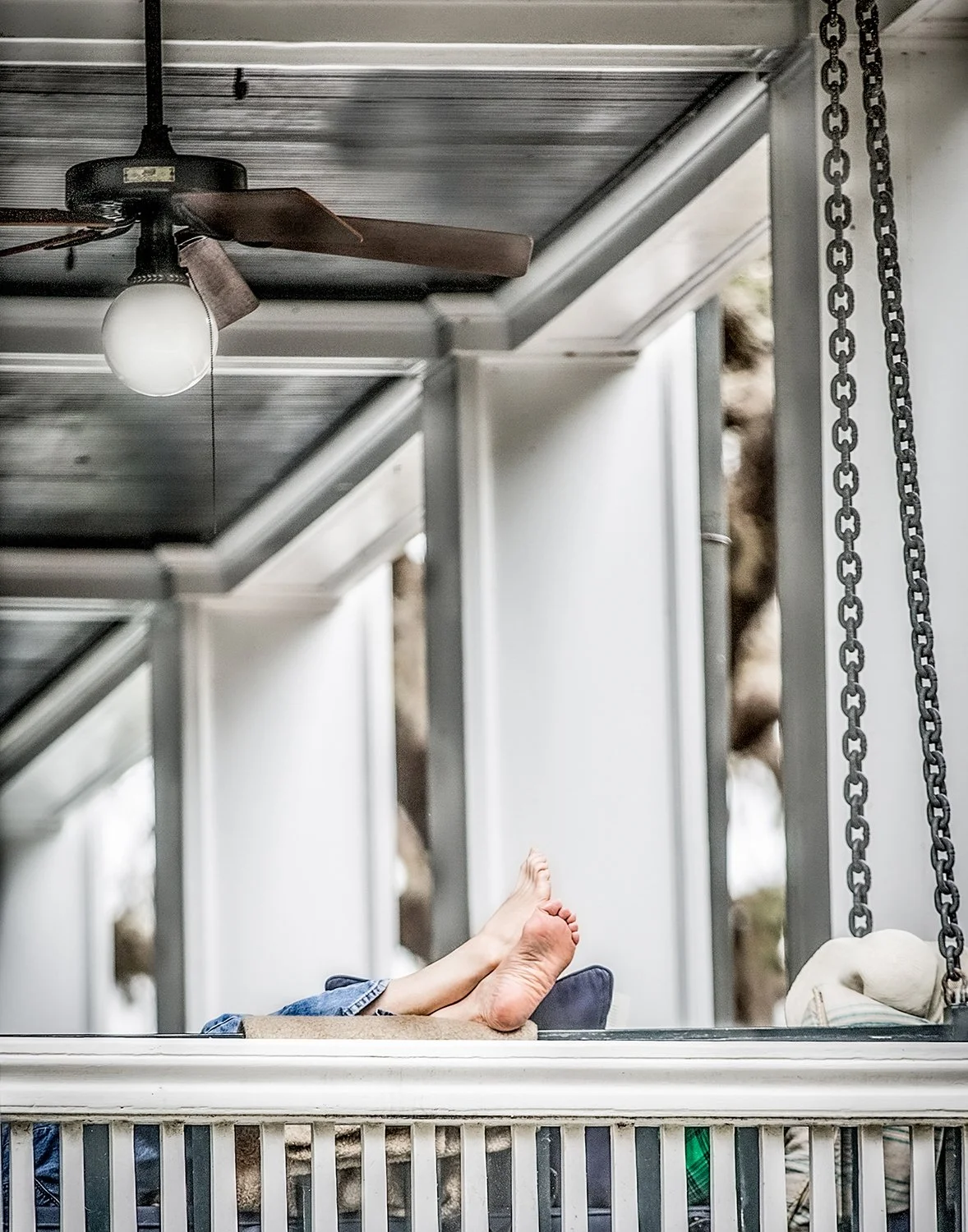 Bare Feet Resting on a Porch Swing Under a Rustic Ceiling Fan