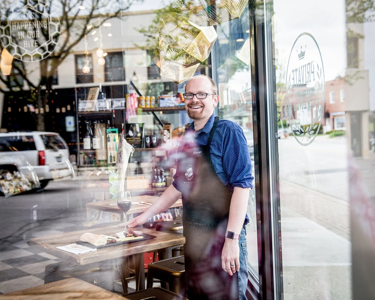 Small Business Branding and Restaurant Photography Capturing a Worker Standing by a Table with Wine and Charcuterie, Viewed Through a Window