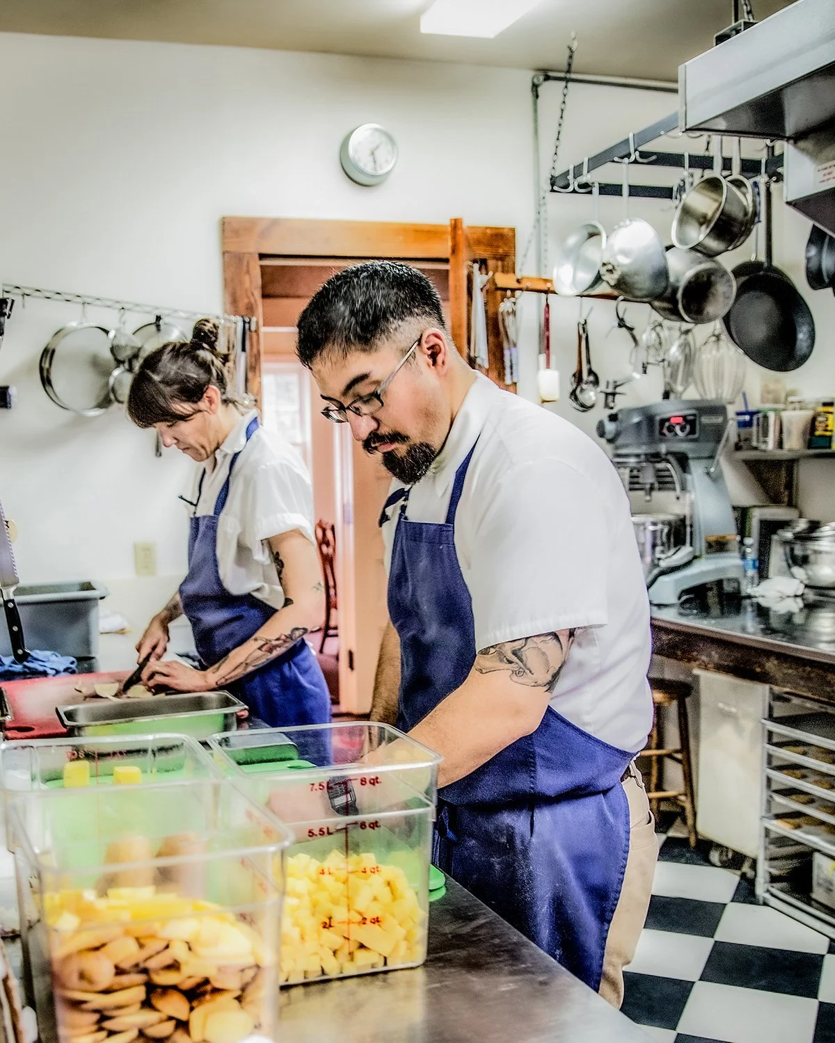 Culinary Lifestyle Photography Showing Two Chefs in Blue Aprons Prepping Ingredients on a Stainless Steel Counter in a Commercial Kitchen