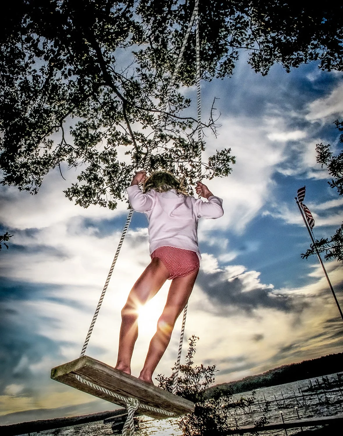 Low-Angle Lifestyle Photography of a Young Girl Swinging on a Tree Swing against a Dramatic Sunset
