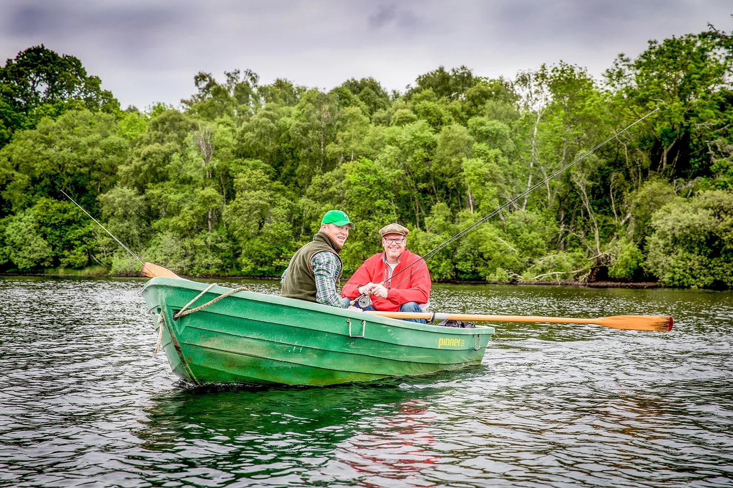 On-Location Lifestyle Photography of Two Fishermen with Fly Rods in a Small Boat Surrounded by Dense Forest