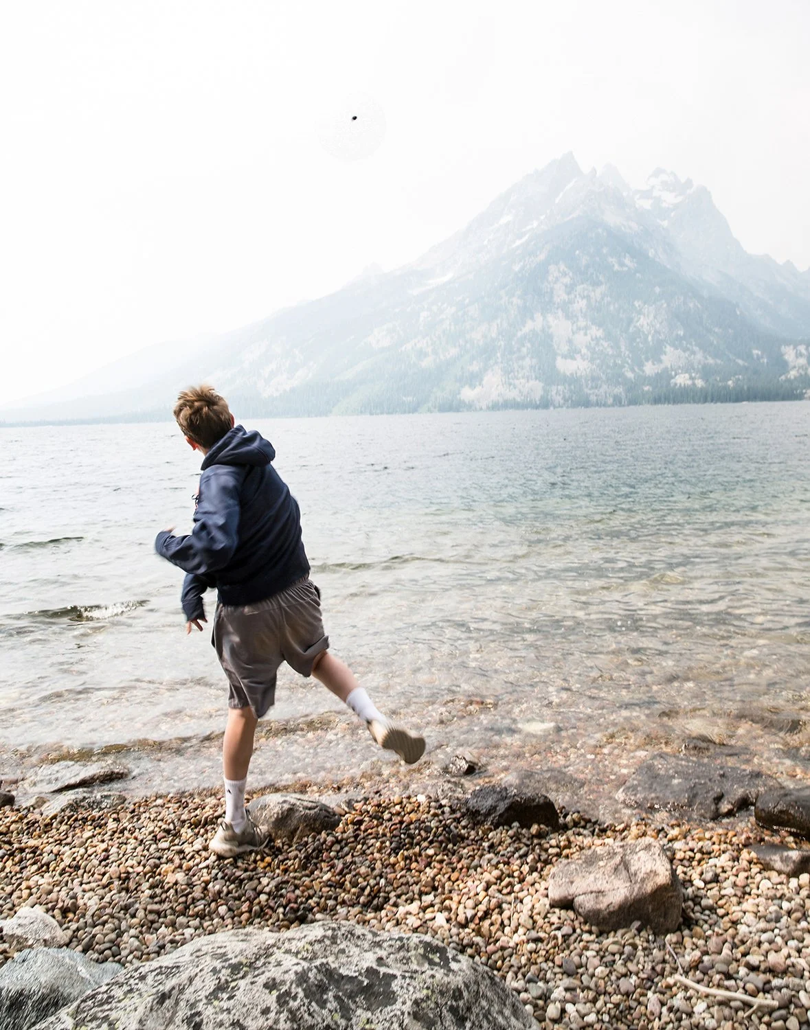 Adventure Lifestyle Photography of a Boy Skipping Rocks at a Scenic Mountain Lake