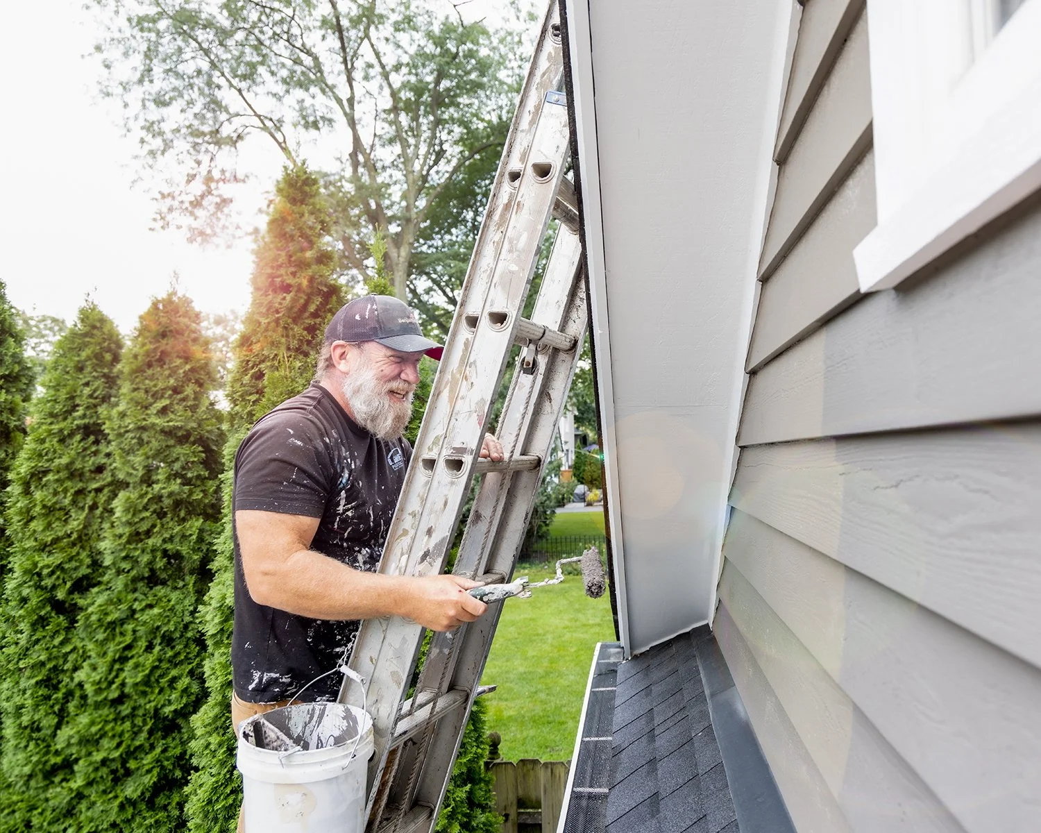 Bearded Man on Ladder Painting a Garage