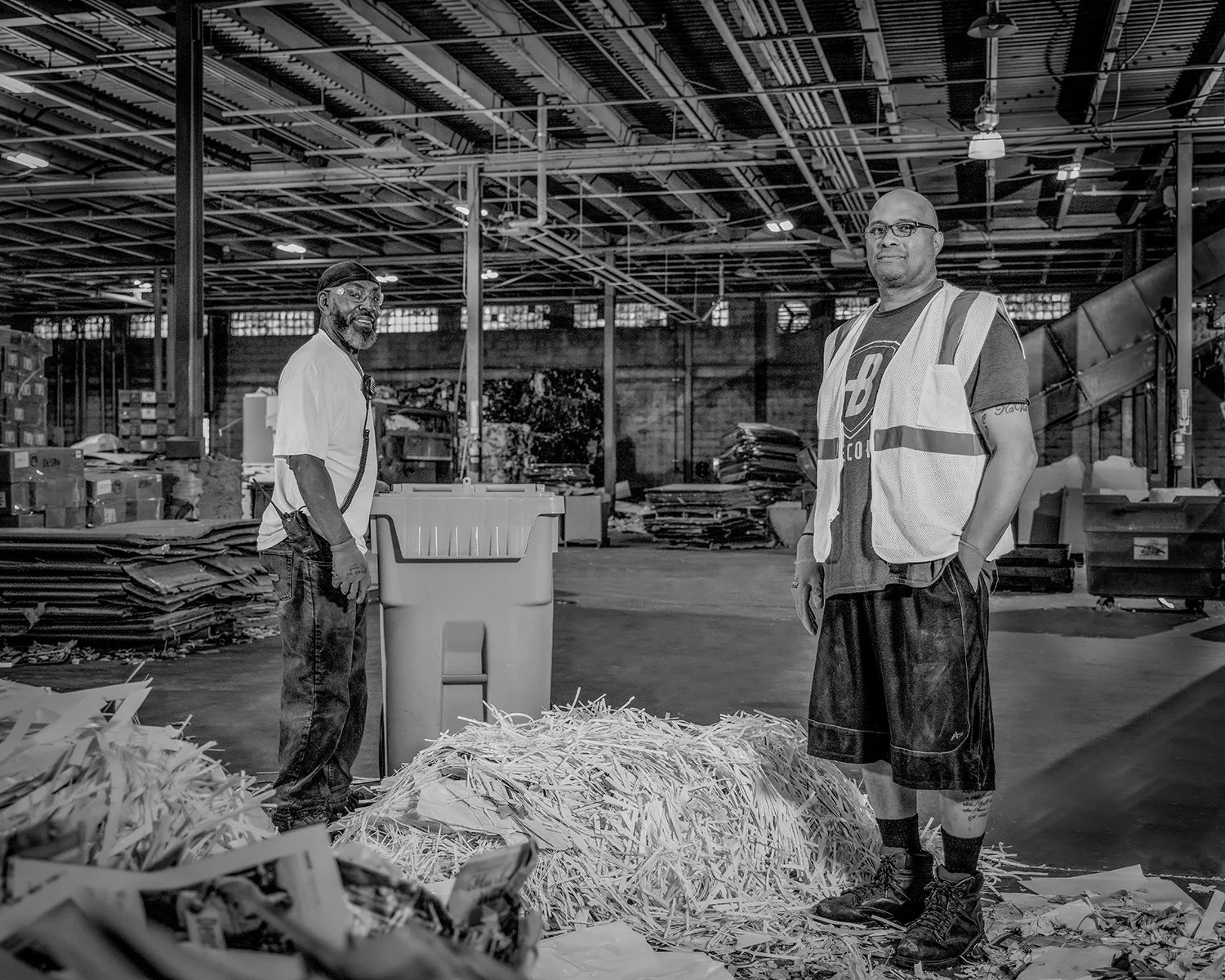 Portrait of 2 Men Among Piles of Paper in Recycling Plant