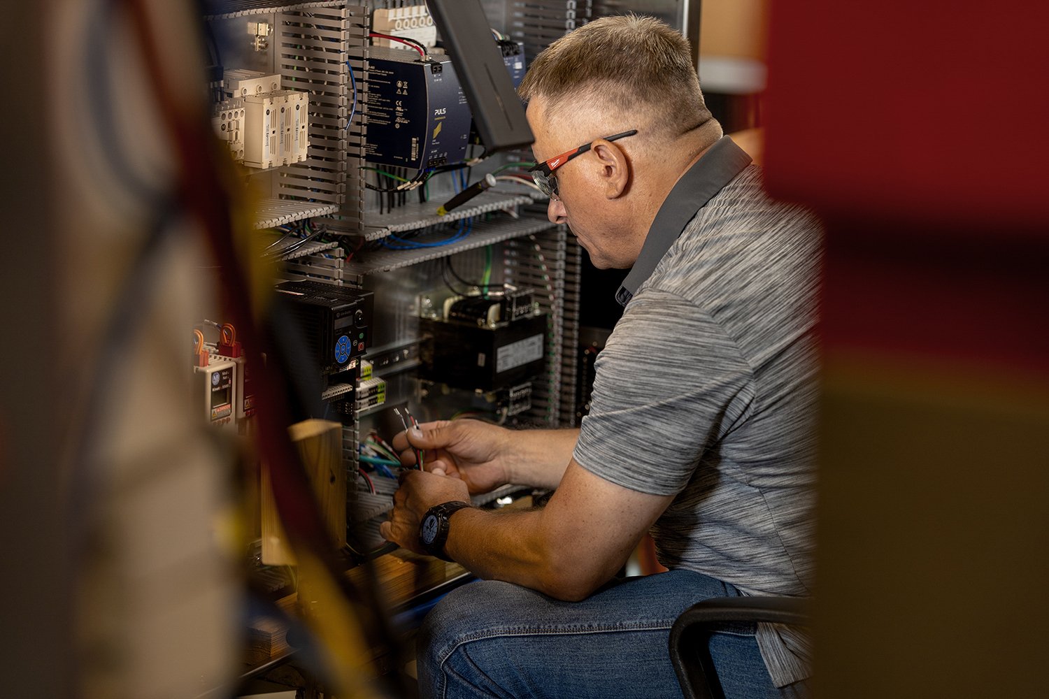Chicago Industrial Photography of An Electrical Technician Wearing Safety Glasses Assembles Wires Inside a Complex Control Panel