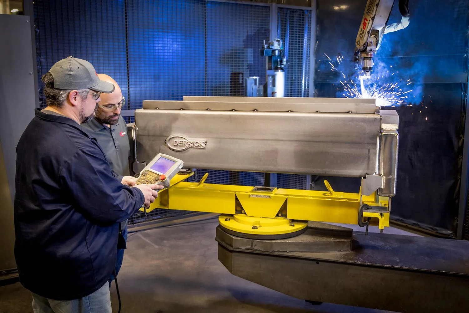 Industrial Commercial Photography of Engineers Using a Digital Pendant to Control a Robotic Welding Cell in a Modern Factory