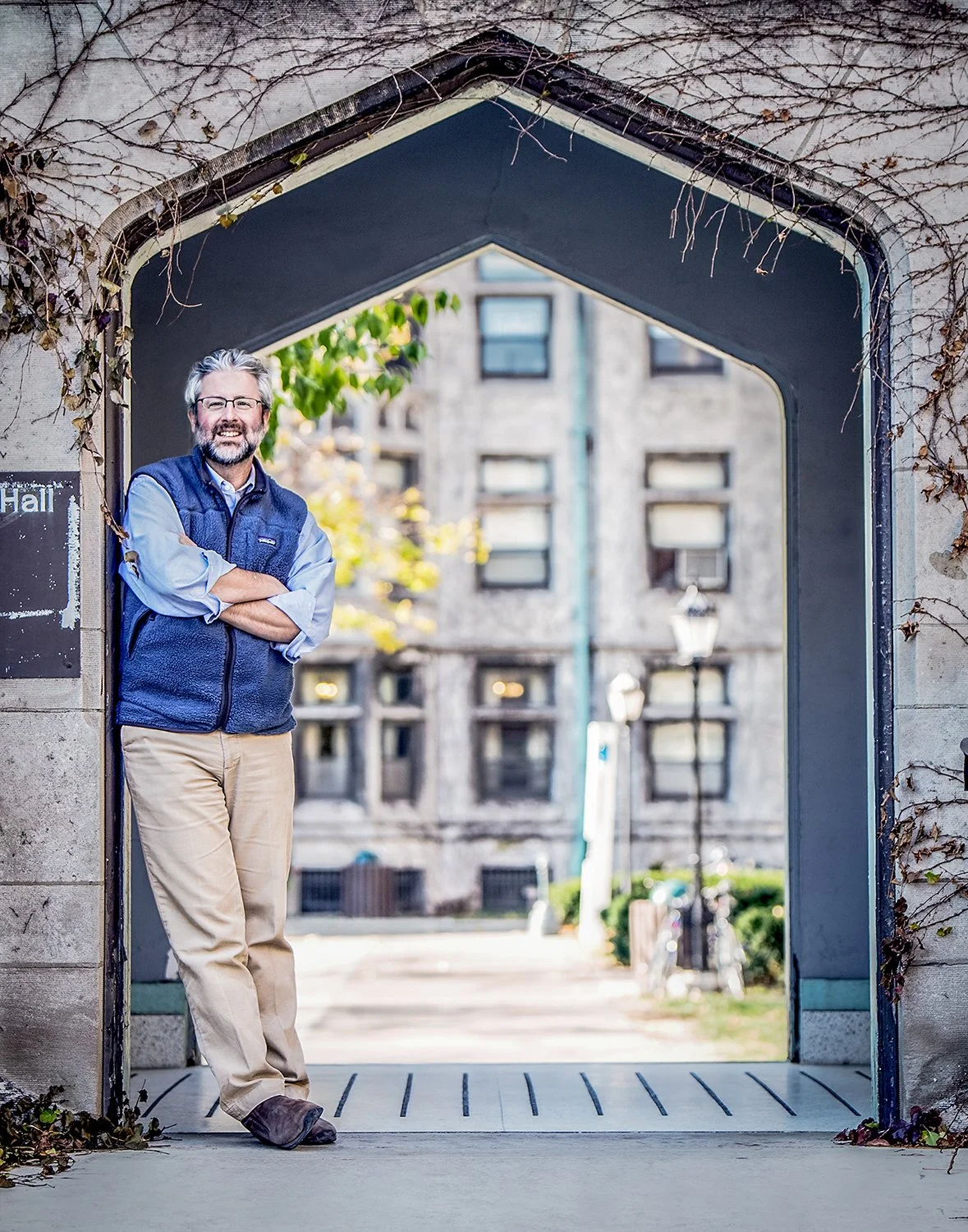 Smiling Man with Glasses and a Fleece Vest Posing Under a Gothic Stone Arch