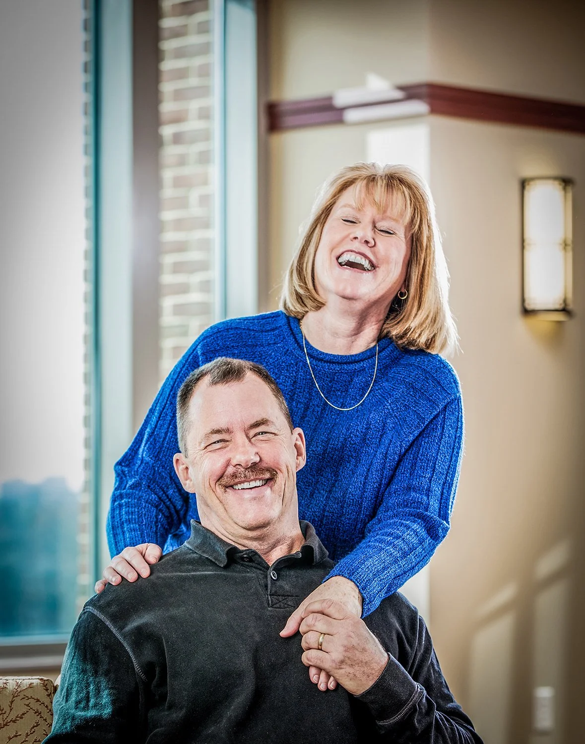 Happy Couple Laughing in Hospital Waiting Area for Healthcare Marketing Campaign