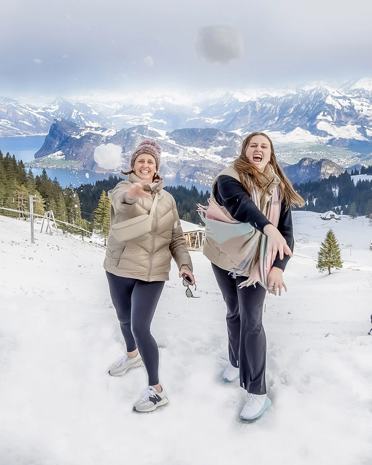 Mother and Daughter in Winter Scene with Mountains in Background Throwing Snowballs at the Camera