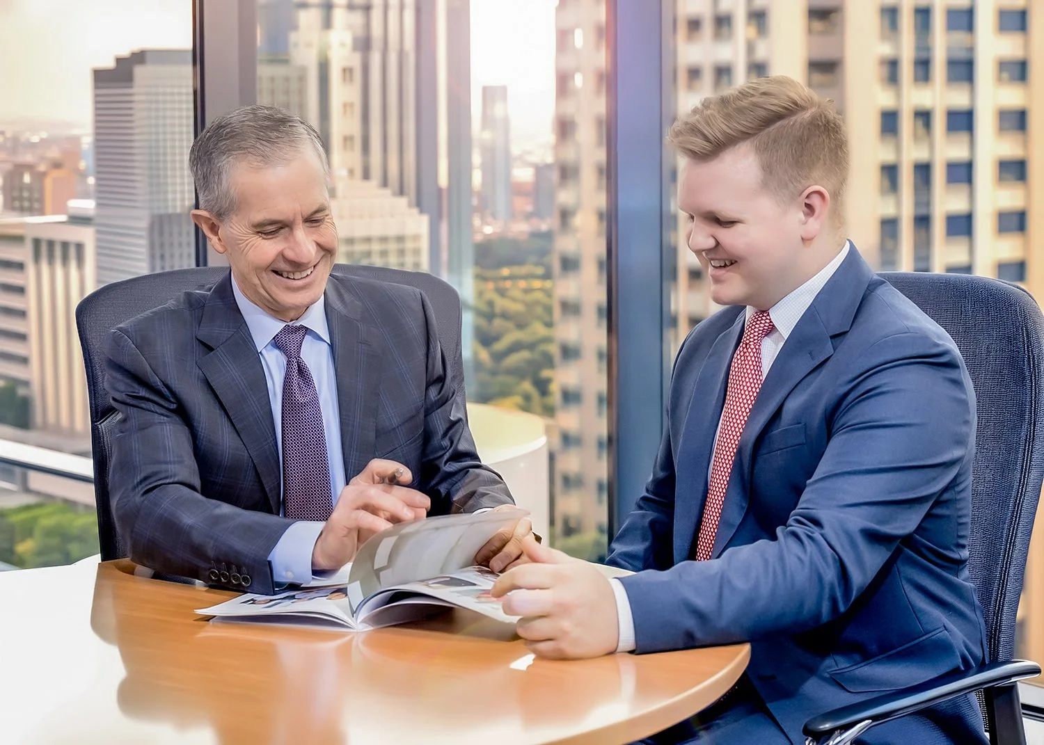 Corporate Lifestyle Photography of Two Businessmen Smiling and Reviewing a Brochure in a Modern High-Rise Office
