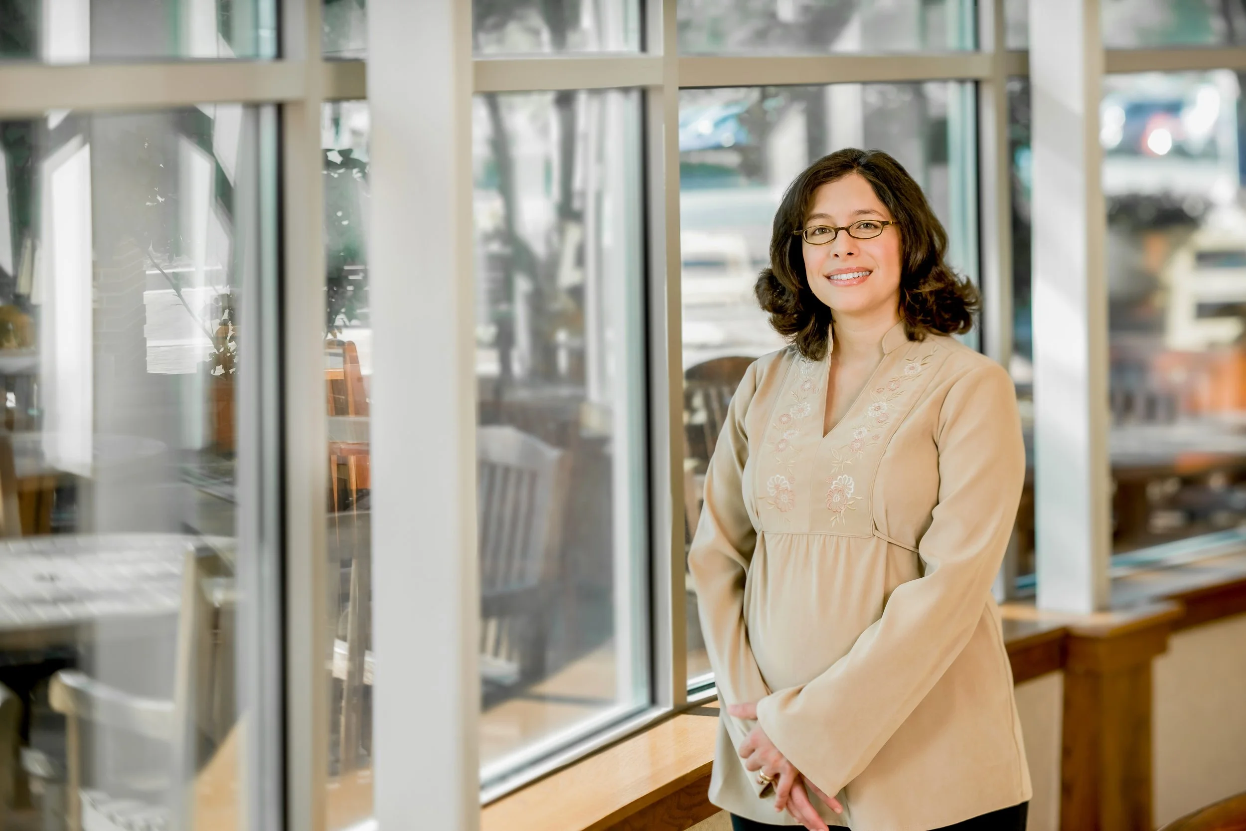 Female with Dark Hair and Glasses Crossing Her Arms in Front of Large Windows