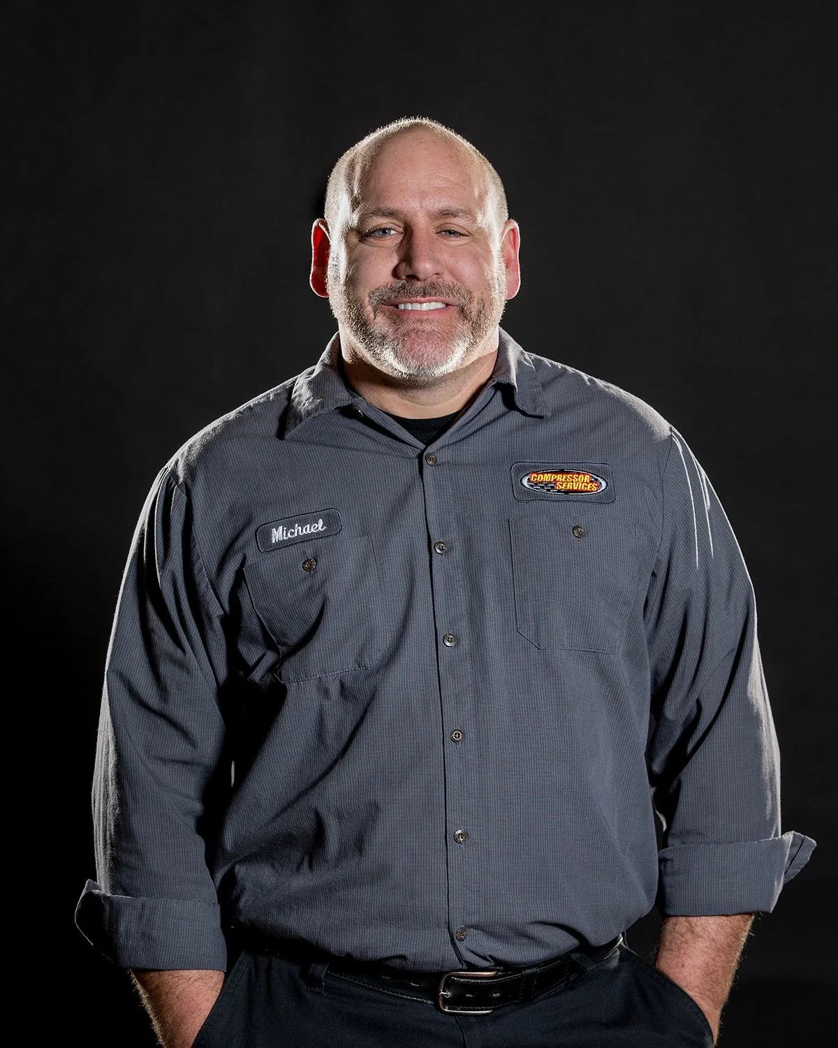 Corporate Headshot of Service Technician Smiling against a Solid Black Background with Dramatic Rim Lighting