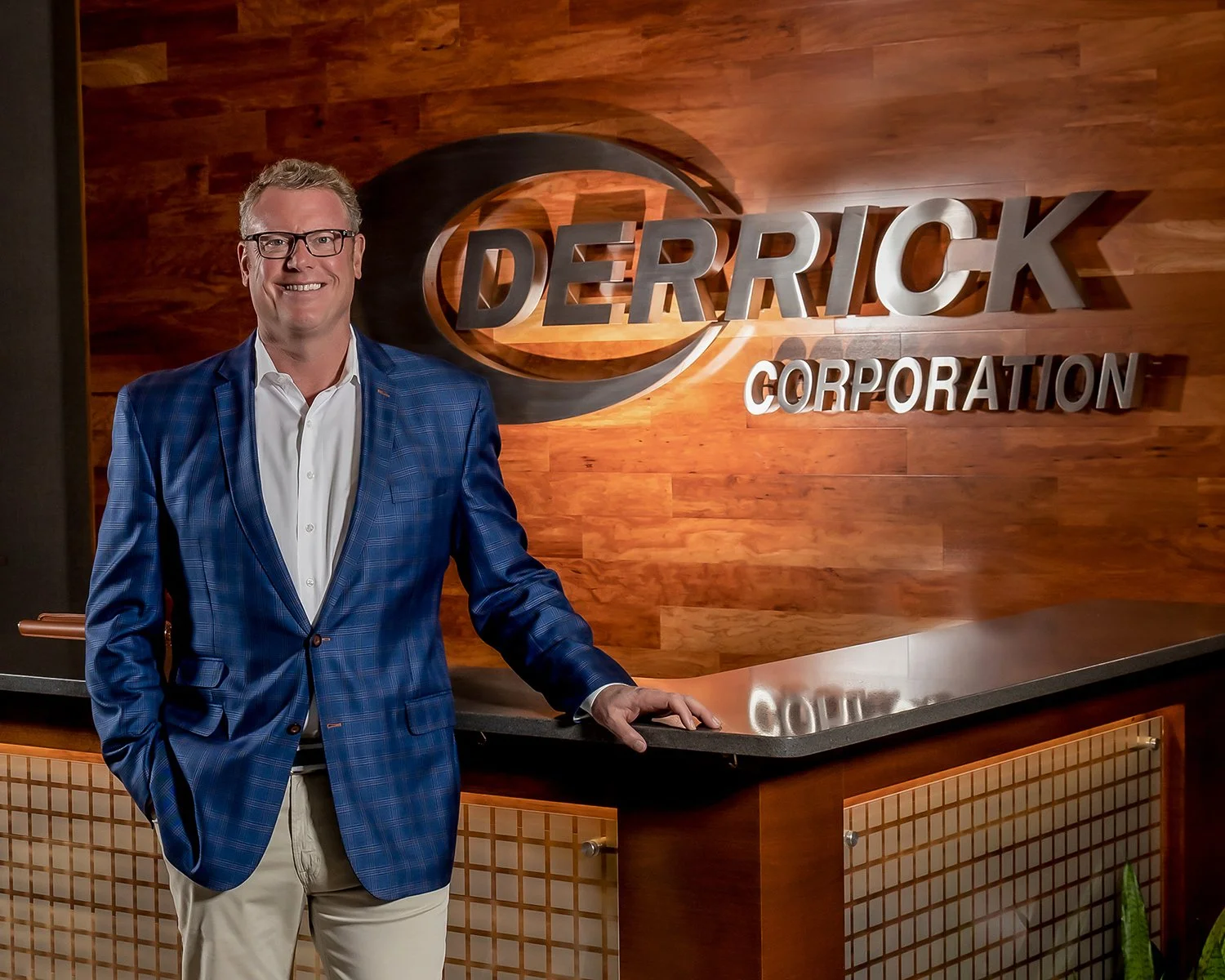 Corporate Environmental Portrait of a Smiling Executive in a Blue Patterned Blazer at a Modern Wood-Paneled Reception Desk