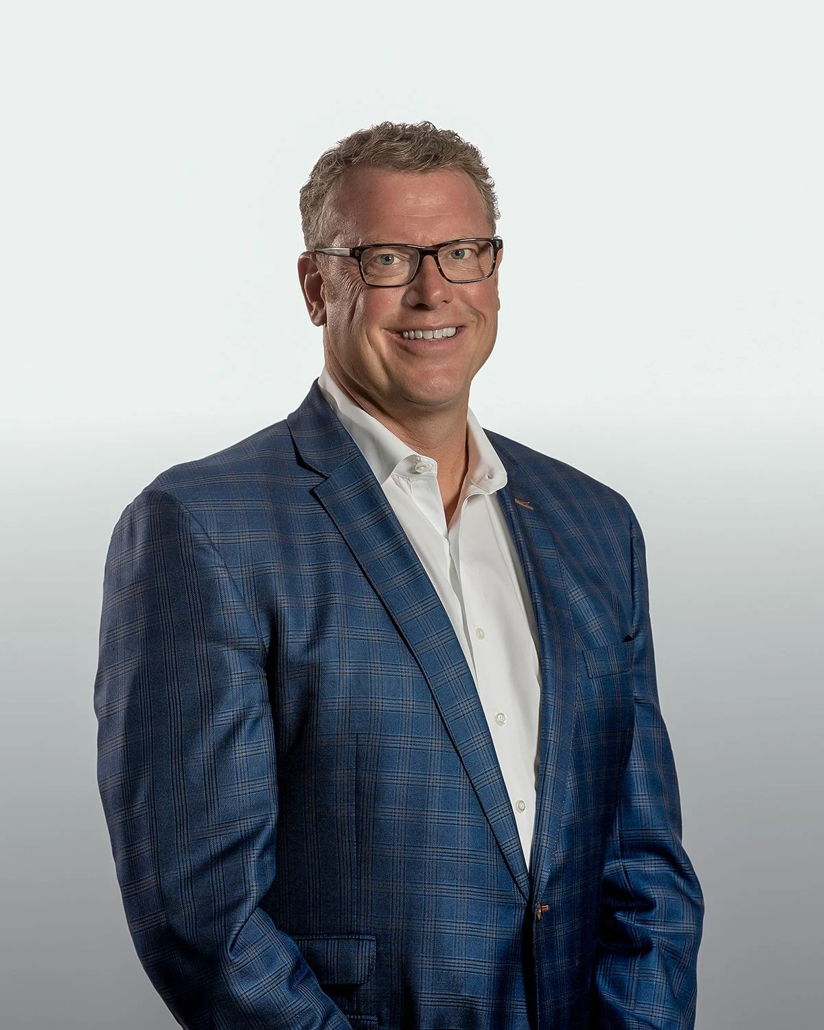 Professional Corporate Headshot of a Smiling Man in a Blue Plaid Blazer against a Gradient Gray Background