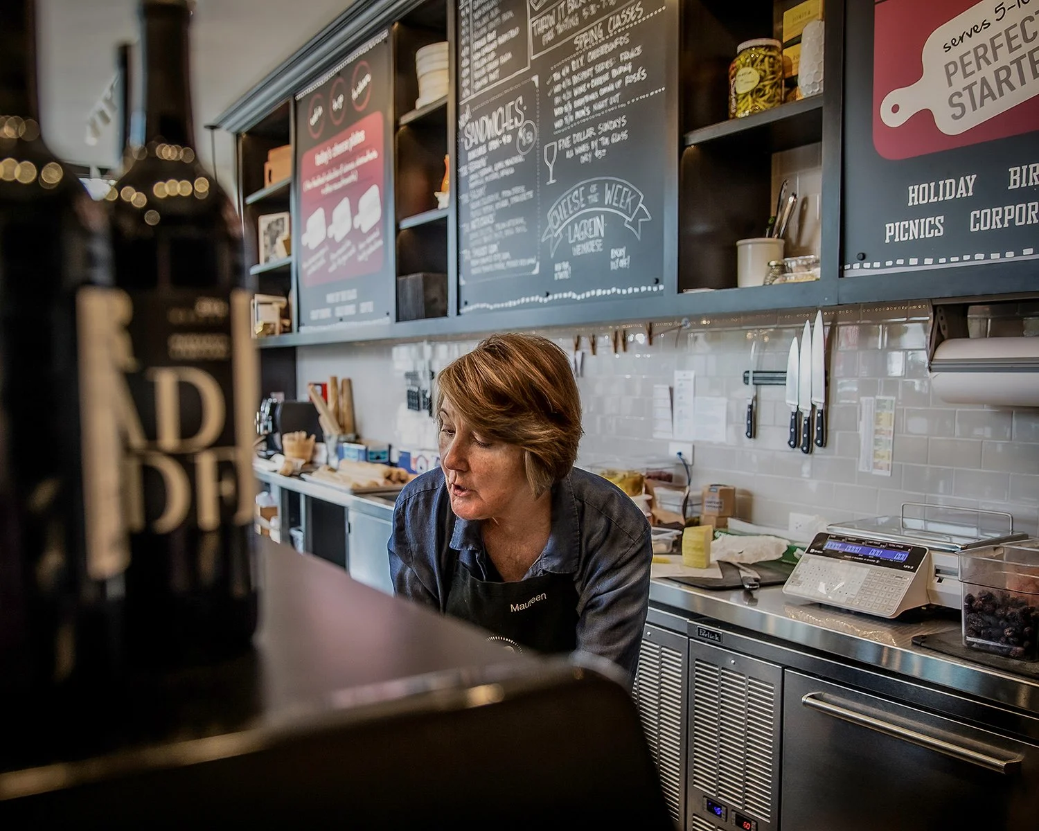Woman Helping a Customer in a Gourmet Cheese and Charcuterie Shop.  Restaurant Photography