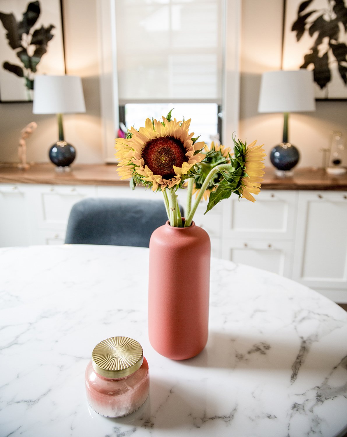Sunflowers in a Terracotta Pink Ceramic Vase Resting on a White Marble Table Alongside a Candle