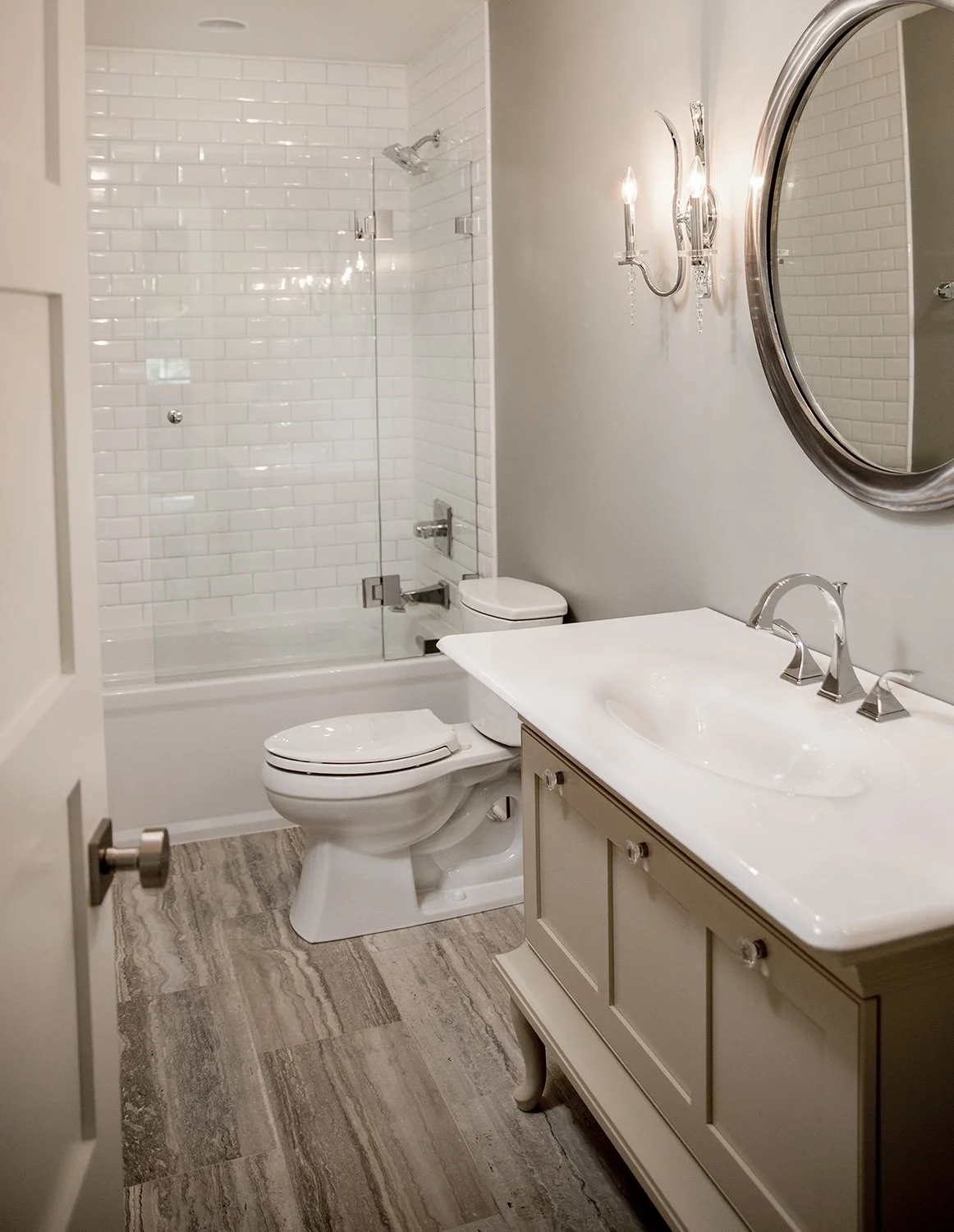 Bright Bathroom Interior with a White Subway Tile Shower, Neutral Vanity, and an Oval Silver Mirror