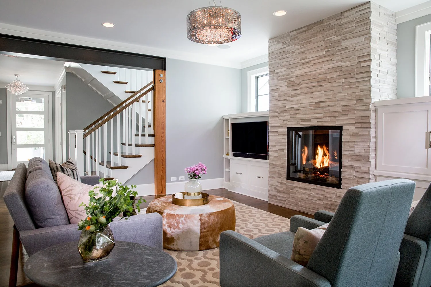 Modern Living Room Interior with a Stacked Stone Fireplace with a Lit Fire, a Cowhide Ottoman, and Gray Sofas