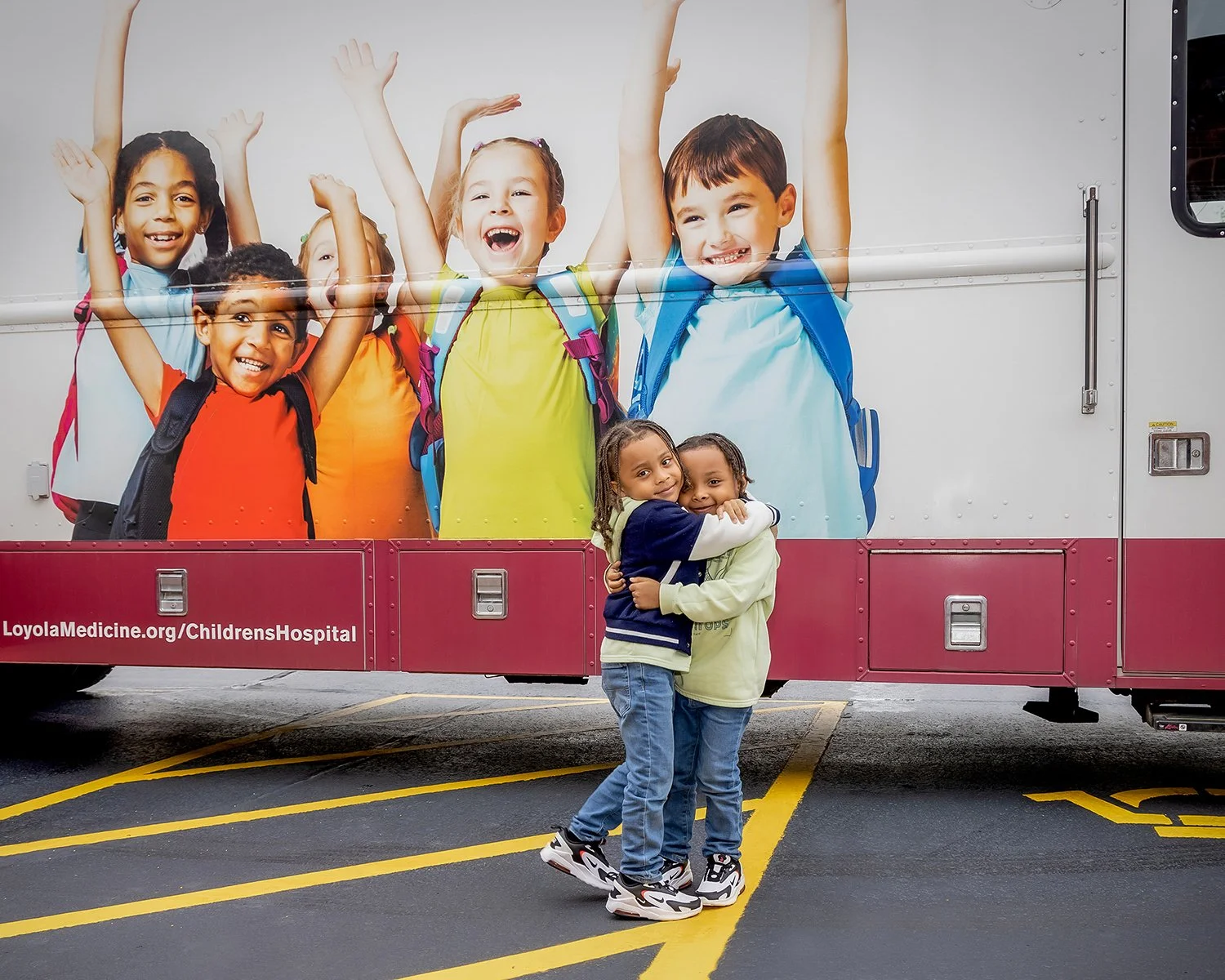 2 Young African American Boys Hugging Each Other in front of a Van with Kids Painted on the Side of it Laughing and Smiling