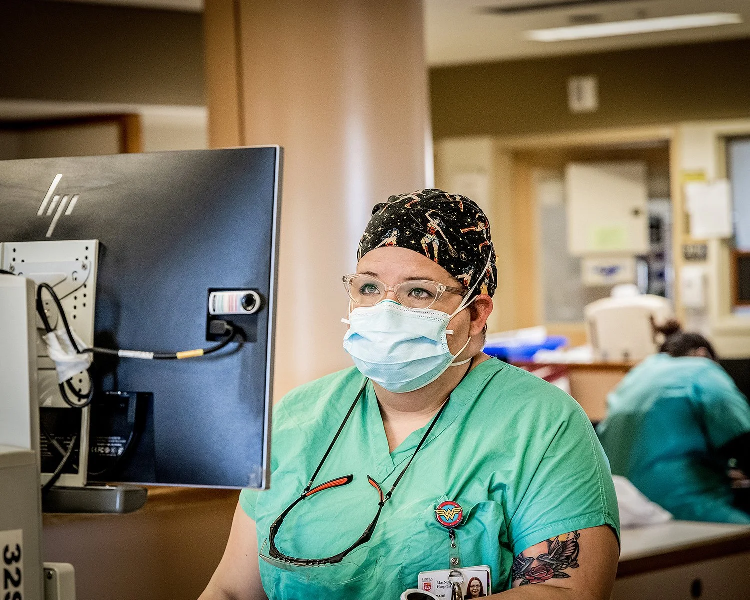 Female Nurse in Scrubs Wearing a Mask Working on a Computer in Medical Environment