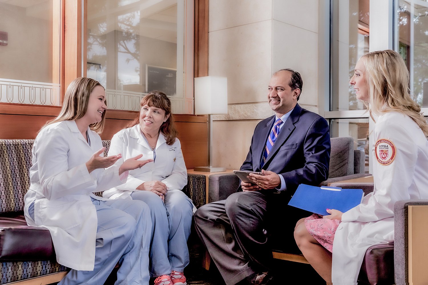 Indian Doctor Holding a Tablet and Talking with 3 Nurses in White Lab Coats in a Hotel Lobby