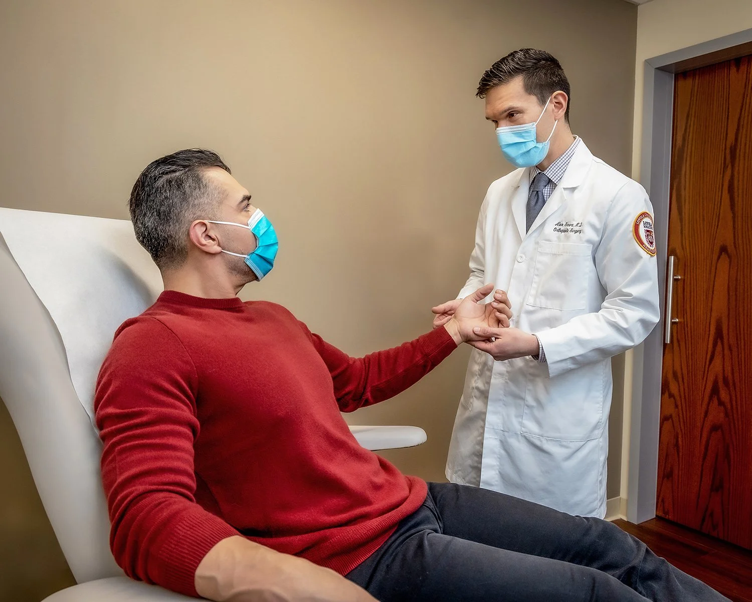 Male Doctor Wearing White Lab Coat and Mask Examining Male Patients Hand in Doctors Office