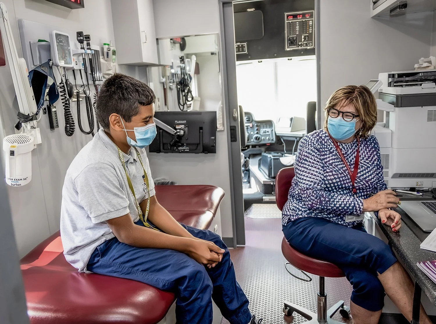 Young Latino Boy Wearing a Mask but Laughing while Female Medical Staff Admits him for Treatment in Pediatric Mobile Health Unit.  Medical Lifestyle Photography