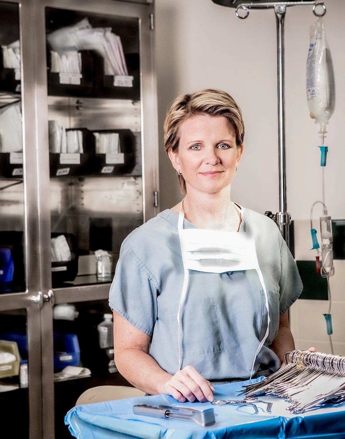 Portrait of Female Nurse with Medical Supply Cabinet and IV Drip in Background.  Surgical Tools on Surface in Front