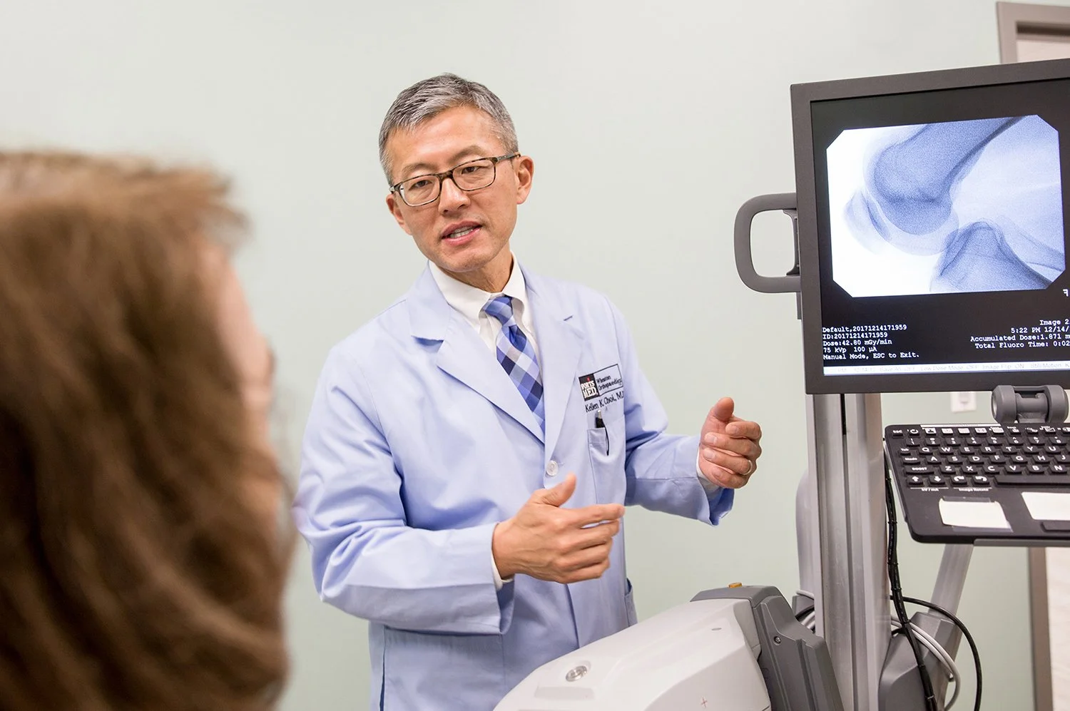 Asian Doctor in Blue Lab Coat Explaining Knee Xrays to his Female Patient