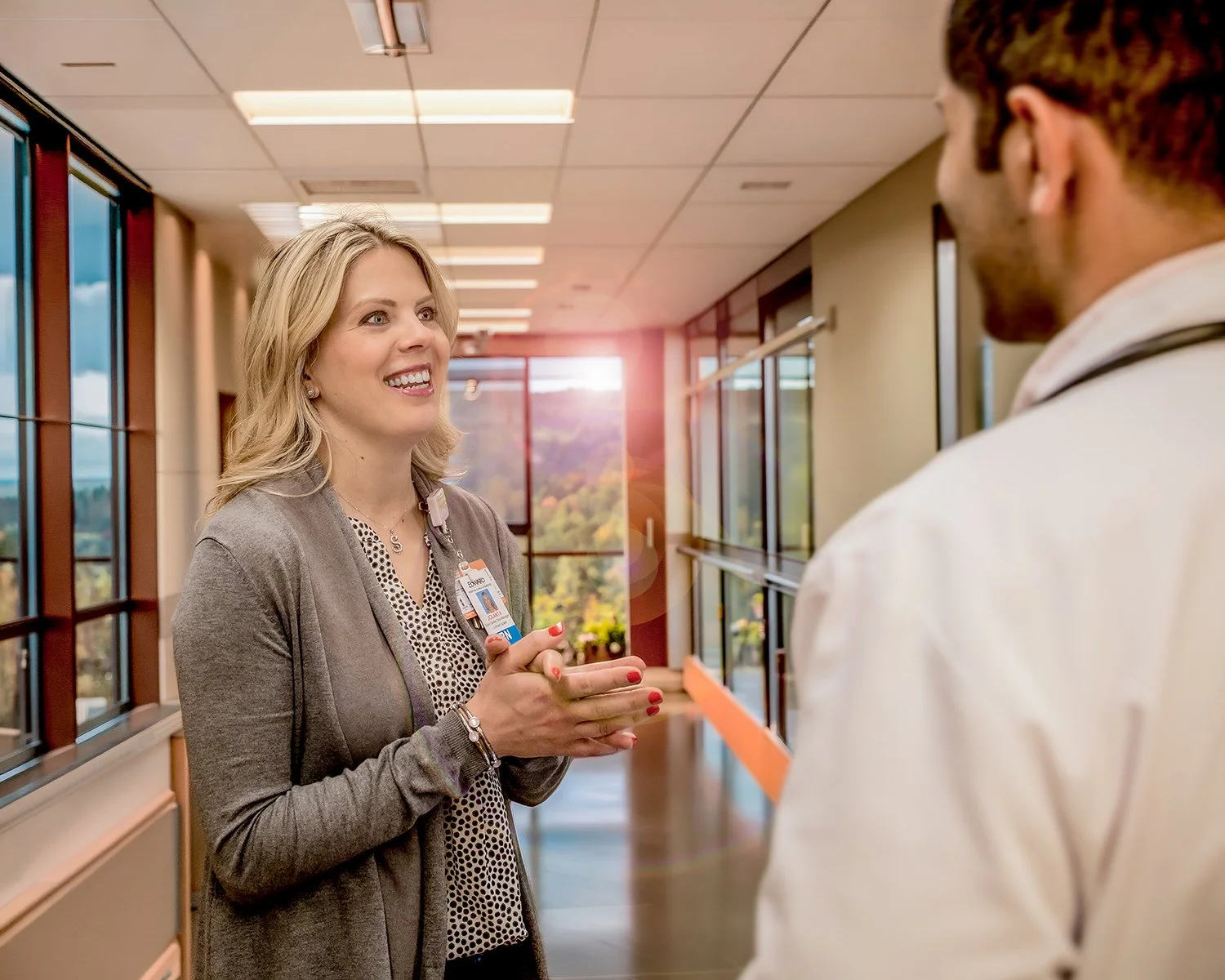 Female Medical Staff Talking with Male Doctor in Modern Hallway with Lots of Windows