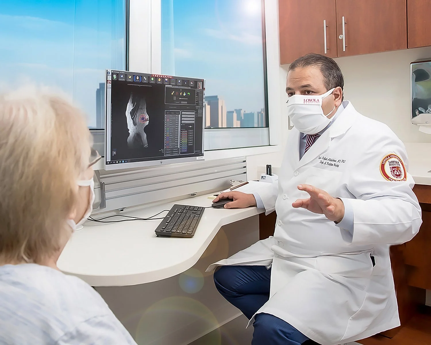 Cancer Doctor in White Coat and Patient in Medical Office During Consult with Computer and Big Window