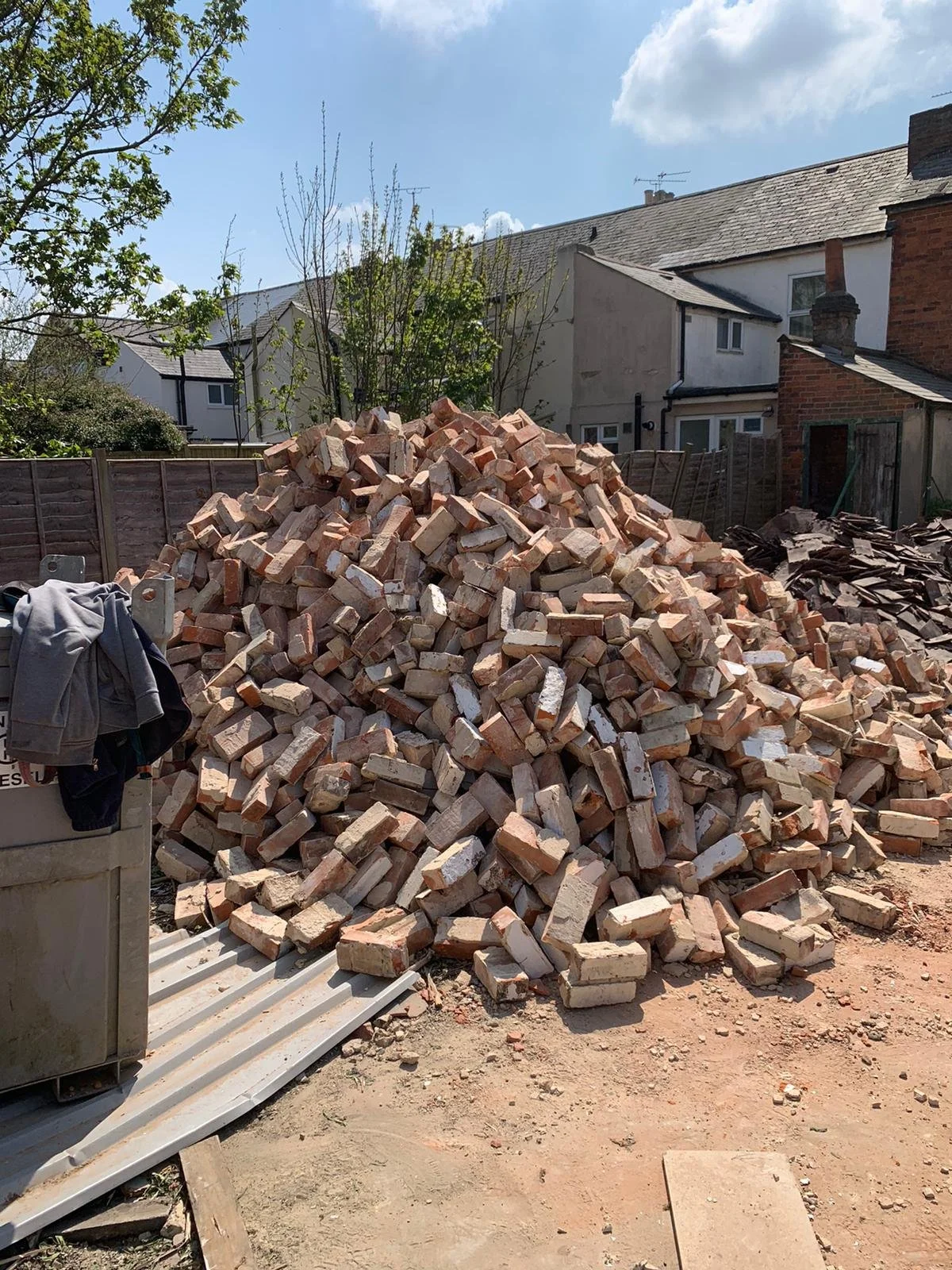 Large pile of bricks on a construction site with buildings and trees in the background.