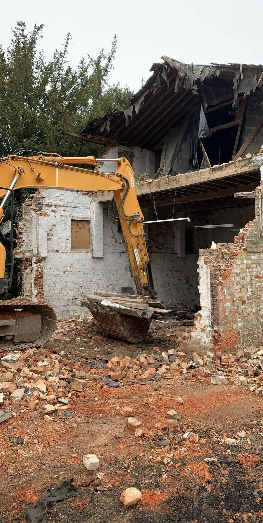 Yellow excavator conducting structural demolition and site clearance work.