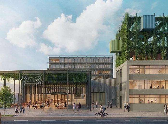 Moderne Architektur mit mehreren Gebäuden, Menschen vor einem Café, Fahrradfahrer auf der Straße, klarer Himmel mit Wolken.