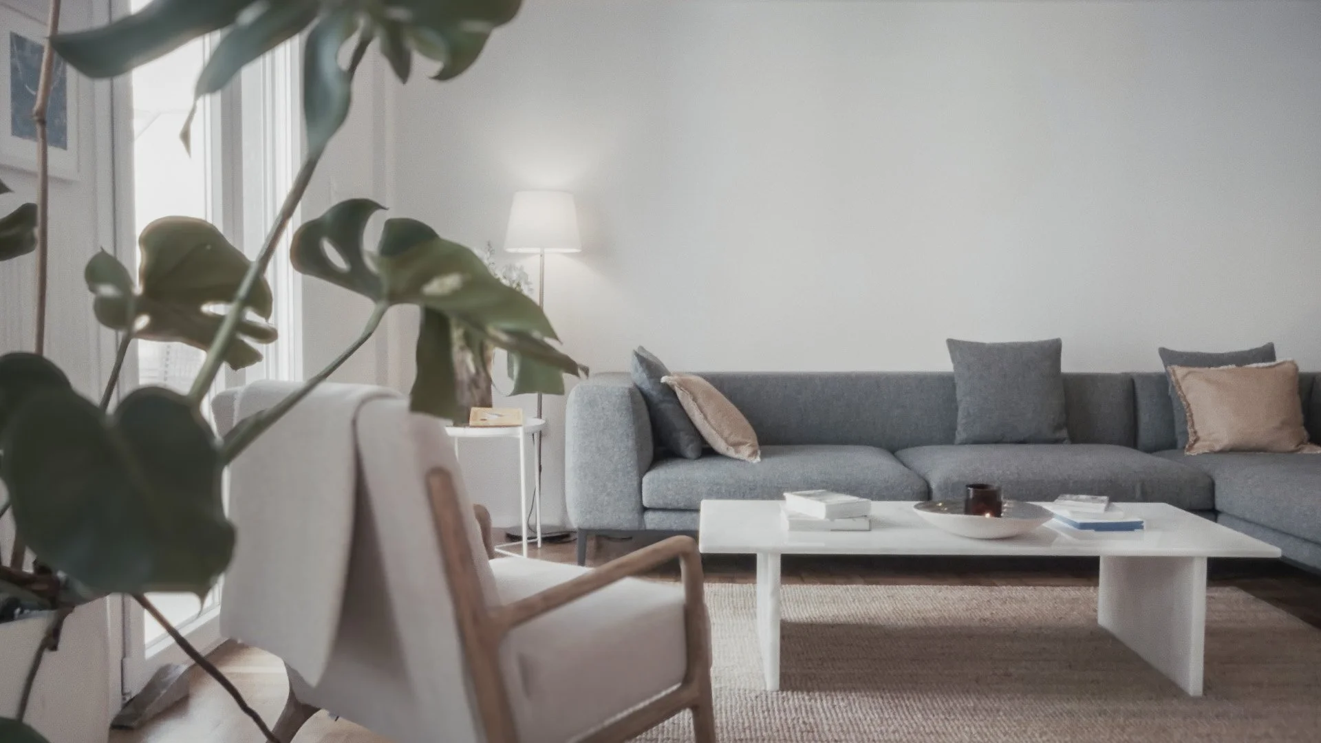 Modern living room with gray couch, decorative pillows, white coffee table, and a side table with a lamp in a bright space.