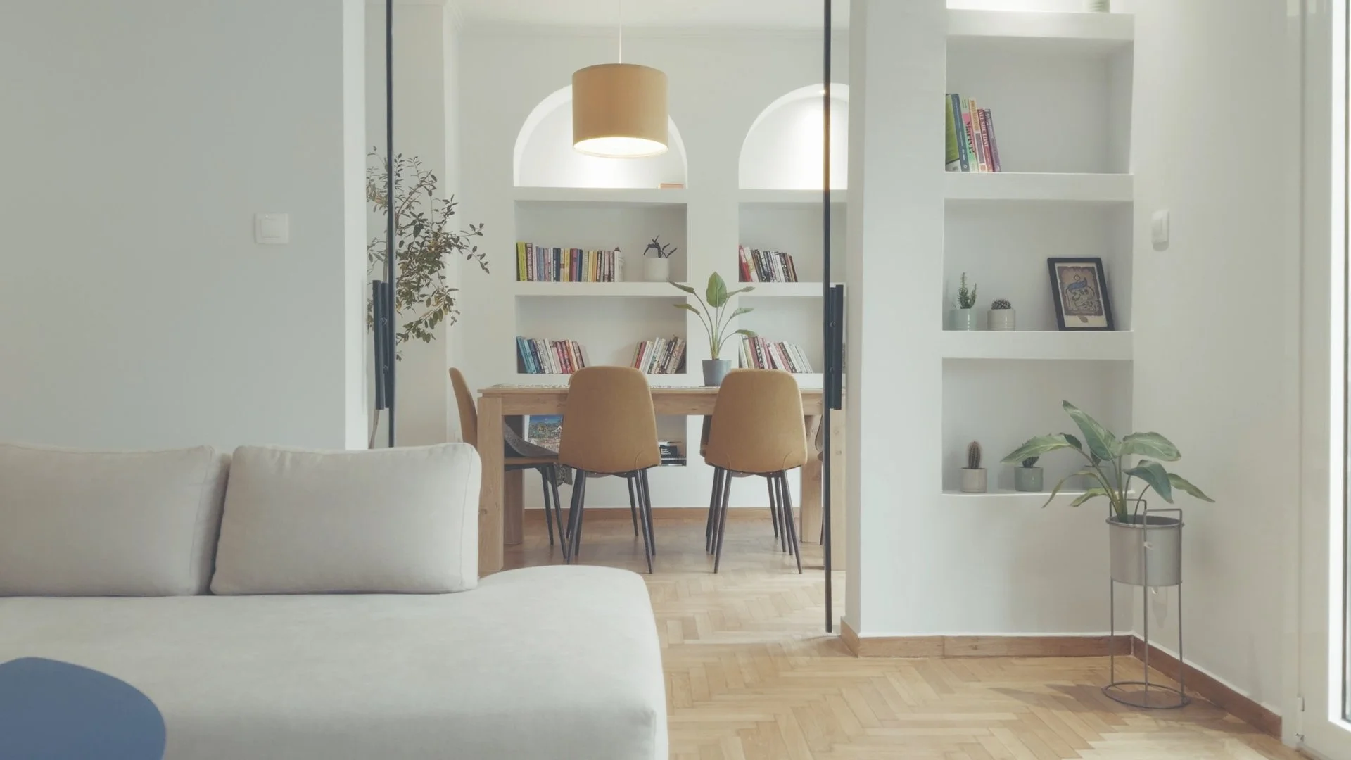 Living room view into dining area with bookshelves, a dining table, and chairs; cozy and modern decor with plants and framed art.