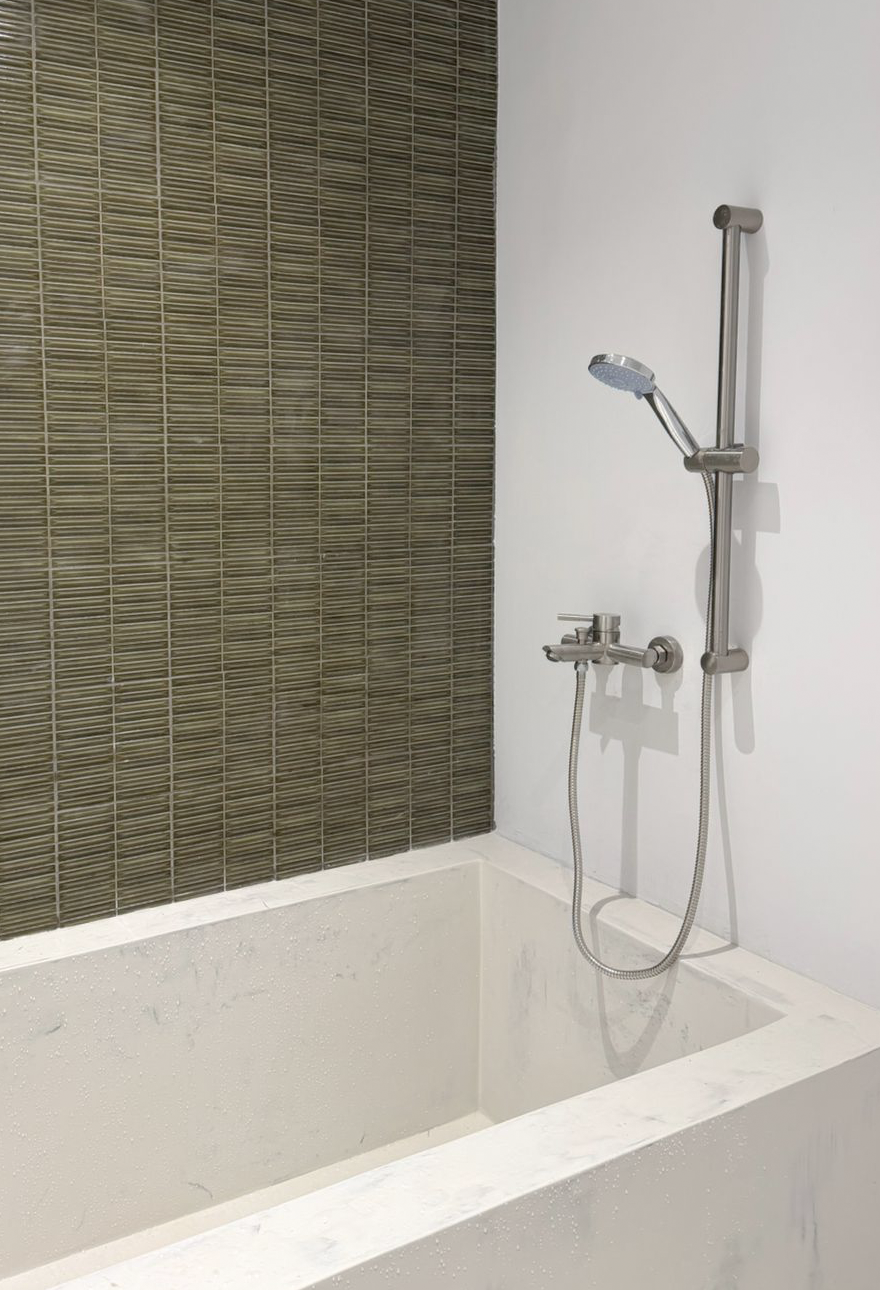 Modern bathroom with a white bathtub, brown tiled wall, and metal shower fixtures including a handheld showerhead on a sliding bar.