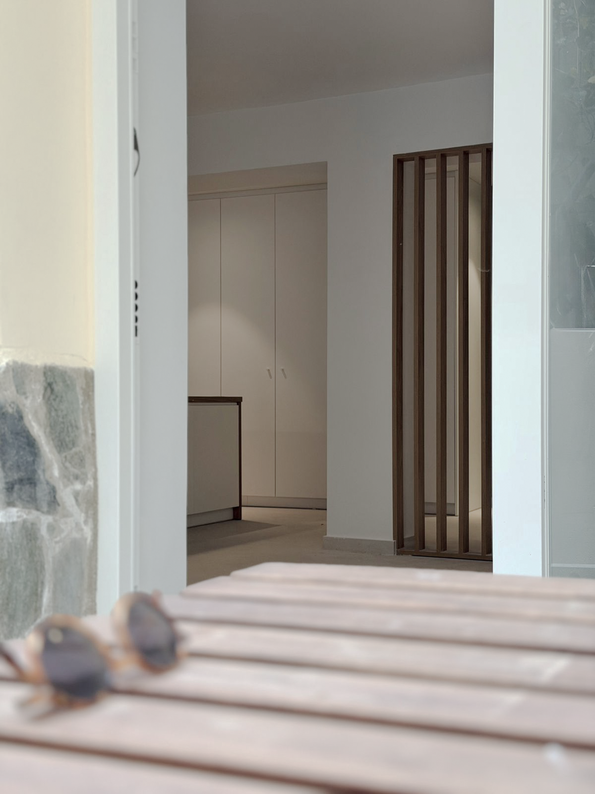 Interior view of a modern home with white walls, wooden slatted room divider, cabinet, and stone accents visible.